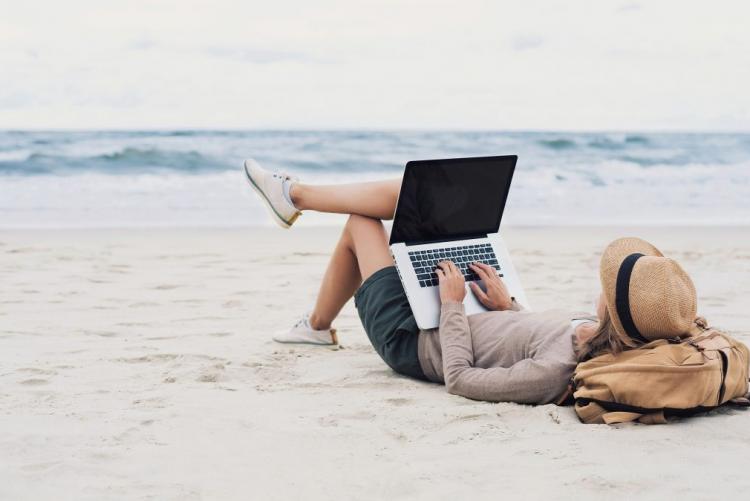 jeune fille allongée sur la plage travaillant sur un PC 