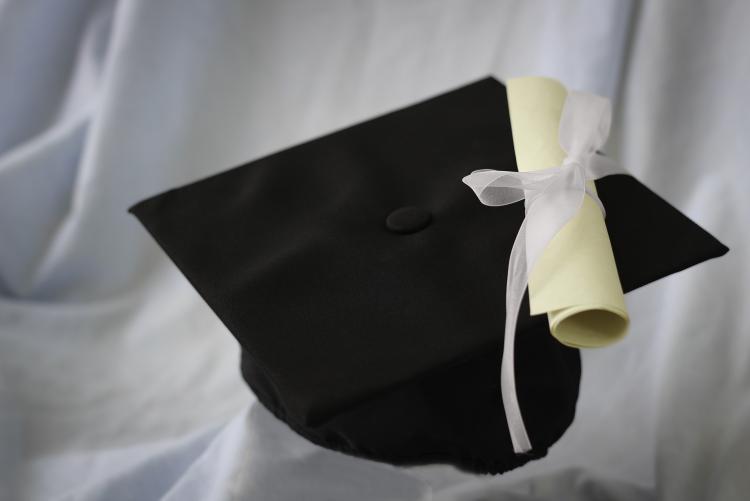 photo du bonnet de graduation noir placé sur un drap blanc avec diplôme enroulé et noué d'un ruban blanc blanc