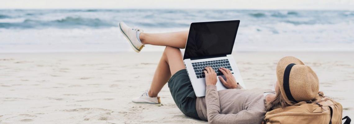 jeune fille allongée sur la plage travaillant sur un PC 