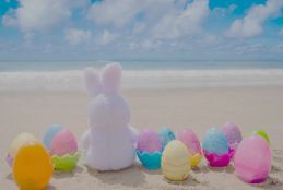lapin en peluche sur une plage entouré d'œufs de Pâques colorés