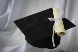 photo du bonnet de graduation noir placé sur un drap blanc avec diplôme enroulé et noué d'un ruban blanc blanc